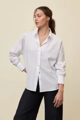 Camisa blanca de manga larga con cierre frontal de botones de nácar, cuello camisero y corte holgado.