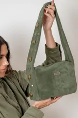 Cartera de hombro confeccionada en gamuza color verde oliva, con correa ancha decorada con tachas metálicas doradas de distintos tamaños. Presenta cierre superior y placa metálica con el logo de la marca en el frente.
