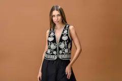 Chaleco de terciopelo negro con escote en V profundo, adornado con bordados florales en hilo plateado y detalles de cuentas. Presenta un diseño sin mangas con ribetes a juego en los bordes.