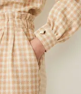 Short tipo clochard de tiro alto confeccionado en tejido tweed con estampado cuadrillé en tonos beige y crema. Presenta cintura elástica, bolsillos laterales y detalle de botones metalizados frontales.