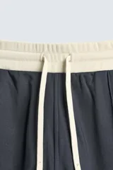 Pantalón jogger de corte wide fit en tejido compacto color gris oscuro. Presenta cintura elástica con cordón ajustable, bandas laterales en contraste color beige y costuras frontales tipo pinza.