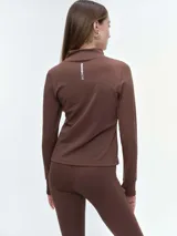 Campera deportiva de cuello alto con cierre frontal de doble cursor. Presenta un corte ajustado que realza la silueta, bolsillos laterales con cierre y mangas largas con puños con abertura para el pulgar.