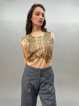 Remera negra de algodón con estampado dorado que simula un tejido o collar sobrepuesto. Presenta una moldería que realza los hombros y se entalla levemente hacia la cintura.