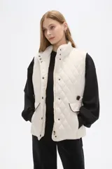 Chaleco acolchado de diseño capitoneado con cierre frontal y botones a presión. Presenta cuello alto, bolsillos laterales con solapa y detalles en contraste en los bordes.