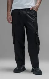 Pantalón cargo de corte oversize y silueta estructurada, confeccionado en microfibra pesada con leve elasticidad. Presenta cintura elástica con cordón de ajuste externo, cierre frontal con botón metálico, bolsillos laterales y bolsillos cargo de gran tamaño con tapa y broches a presión.