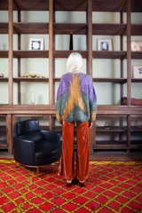 Sweater de lana merino tejido artesanalmente, con diseño pintado a mano que combina tonos violeta, verde y naranja. Presenta cuello redondo, mangas largas y un corte holgado y cómodo.