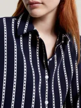 Camisa azul marino con rayas verticales blancas con rombos argyle, de corte amplio, cuello inglés y mangas largas con puños.