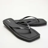 Chanclas de dedo color negro con suela plana y tiras finas.