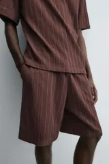 Bermuda de corte relajado color marrón oscuro, confeccionada en tejido jacquard con textura acanalada vertical. Presenta cintura elástica ajustable con cordón, bolsillos delanteros y un bolsillo trasero de plastrón.