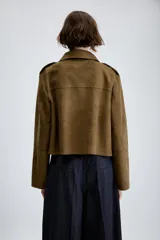 Chaqueta corta de efecto ante en color marrón, con cuello solapa, manga larga y trabillas en los hombros. Presenta cierre frontal con botones y bolsillos delanteros de doble vivo.