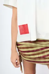 Minifalda de rayas verticales en tonos bordó y beige, confeccionada en tejido elástico con fruncidos laterales regulables mediante cordones.