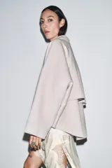 Chaqueta de lana en color beige, con cuello solapa, cierre frontal con cremallera metálica, mangas largas con corte evasé y bajo asimétrico.