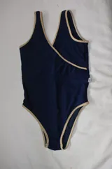 Malla enteriza color azul marino con detalles de ribetes en color beige. Presenta un diseño cruzado en el frente con escote en V y breteles anchos.