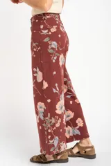 Jean de corte wide leg con tiro medio, confeccionado en algodón peinado. Presenta un diseño estampado con motivos florales sobre una base de color bordó.