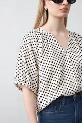 Camisa de viscosa con estampado de lunares pequeños en negro sobre fondo blanco o crema. Presenta escote en V con abertura y botones frontales, y mangas cortas abullonadas.