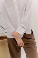 Camisa de manga larga color celeste claro, con cuello camisero y botones frontales. Presenta un detalle de cinta negra alrededor del puño doblado.