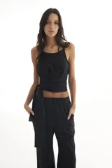 Top negro con acabado brillante, de tirantes finos y diseño cruzado en la cintura con lazo lateral ajustable.