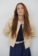 Chaqueta corta color marrón de corte recto, con cuello redondo, cierre frontal de botones y bolsillos frontales tipo parche.