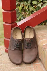 Zapato acordonado de cuero color marrón chocolate con acabado natural, suela de EVA y pasadores de cordones negros.