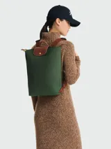 Mochila Longchamp modelo Le Pliage Original tamaño M, color verde oscuro. Presenta solapa y asas de cuero marrón con cierre de botón a presión, correas ajustables de tela y cierre superior con cremallera.