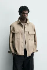 Sobrecamisa relaxed fit color beige con tejido elástico, cuello solapa, manga larga con puños abotonados, bolsillos de plastrón con solapa en el pecho, bolsillos laterales de vivo en la cadera y cierre frontal de botones.