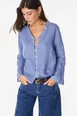 Blusa de lino italiano color beige con escote en V y detalles de volados en el cuello y los puños. Presenta cierre frontal con botones de nácar y mangas largas.