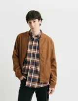 Campera tipo bomber de color marrón, confeccionada en tejido con textura similar a la gamuza, con cierre frontal completo, cuello redondo y puños elásticos.