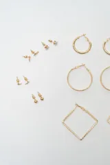 Set de siete pares de aros dorados de diversos diseños, incluyendo aros tipo argolla redondos en dos tamaños, aros cuadrados con textura y varios modelos de aros pequeños tipo broquel con detalles de piedras y esferas.