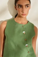 Top de lino blanco sin mangas, con cuello redondo y cierre de botones de madera dispuestos en una cartera asimétrica. Cuenta con delicados detalles bordados en forma de flor alrededor de los ojales.