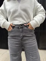 Pantalón de corte recto en color negro, confeccionado en tela elastizada de alta calidad. Presenta un diseño de tiro medio con detalle de tachas metálicas en la zona de los bolsillos delanteros.