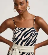 Mono largo de sastrería marca Cortelle, confeccionado en crepé con elastano, con estampado animal print de cebra en tonos beige y negro. Presenta escote recto, tirantes finos regulables, corte wide leg en las piernas y un cinturón ancho ajustable en la cintura.