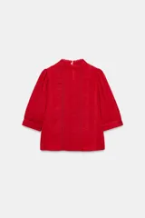 Blusa blanca de cuello alto con detalles de puntilla, manga corta abullonada y cierre posterior con botón.