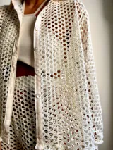 Camisa de playa color crema, de tejido crochet con botones frontales y cuello clásico.