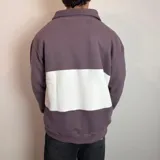 Buzo de algodón con medio cierre frontal y cuello tipo polo. Presenta un diseño de bloques de color en tonos gris oscuro y blanco, con bordados decorativos en el pecho.