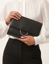 Cartera tipo clutch de cuero sintético negro, con solapa frontal y herraje metálico circular plateado.