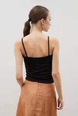 Top de tirantes finos con diseño bicolor, presentando una parte superior con lentejuelas plateadas y un frunce central, y una parte inferior de tela metalizada plateada.