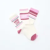 Pack de tres pares de medias de algodón color blanco con puños, talones y punteras en color fucsia. Un par tiene rayas horizontales fucsias y grises, otro tiene la palabra "Enjoy" en fucsia y el tercero tiene la frase "More Love" en fucsia y gris.
