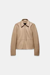 Blazer de cuero color beige con cuello solapa, manga larga y cierre frontal con cremallera y botones a presión ocultos. Presenta bolsillos laterales ocultos en costura y forro interior.