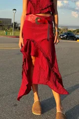 Conjunto de dos piezas compuesto por un top sin mangas con cuello alto y una falda midi asimétrica con volados, ambos confeccionados en seda con textura arrugada.