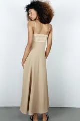 Vestido midi de color beige con escote recto adornado con un panel de encaje semitransparente, tirantes finos ajustables y falda fluida con cierre lateral con cremallera oculta.