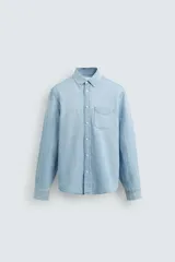 Camisa de corte regular fit confeccionada en denim ligero de algodón con efecto lavado. Presenta cuello solapa con botones, manga larga con puños abotonados, cierre frontal de botones y un bolsillo plastrón en el pecho.