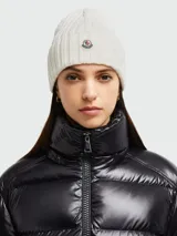 Gorro de lana tejido a punto acanalado, color blanco crudo, con parche circular del logo de Moncler en el frente.