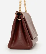 Cartera tipo shoulder bag de tamaño grande, confeccionada en poliuretano con textura de efecto croco. Presenta una solapa frontal con cierre magnético, herrajes en tono dorado claro y una correa de cadena metálica. Incluye un bolsillo interno con cremallera.