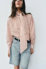 Camisa de rayas rojas y blancas, cuello redondo con lazada integrada y manga larga.