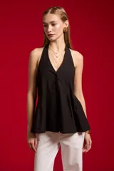 Blusa de algodón color beige con escote en V, cuello halter y cierre frontal con botones. Presenta un diseño ajustado en el torso con pinzas y pliegues en la parte inferior que generan una caída ligeramente acampanada.
