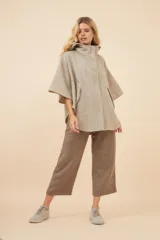 Capa amplia con capucha, confeccionada en lana fina sin teñir. Presenta cierre frontal, bolsillos delanteros y botones laterales que permiten ajustar la forma de las mangas.