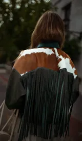 Campera de cuero de silueta oversize y corte corto, con cuello camisero verde oscuro, detalles en pelo de vaca marrón y blanco, y mangas amplias.