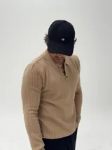 Buzo de tejido de punto color beige, con cuello polo y cierre frontal de tres botones. Presenta una textura acanalada y mangas largas.