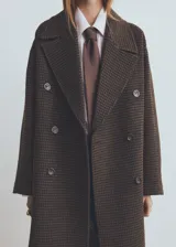 Abrigo de corte sastre con diseño de doble botonadura y solapas amplias. Presenta un estampado de cuadros pequeños en tonos marrones y oscuros, con una silueta estructurada y elegante.