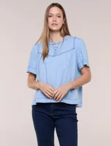 Blusa celeste de lyocell ultraliviano, de estilo romántico y silueta holgada. Presenta escote redondo con abertura en V y botones frontales, canesú fruncido y mangas cortas amplias.